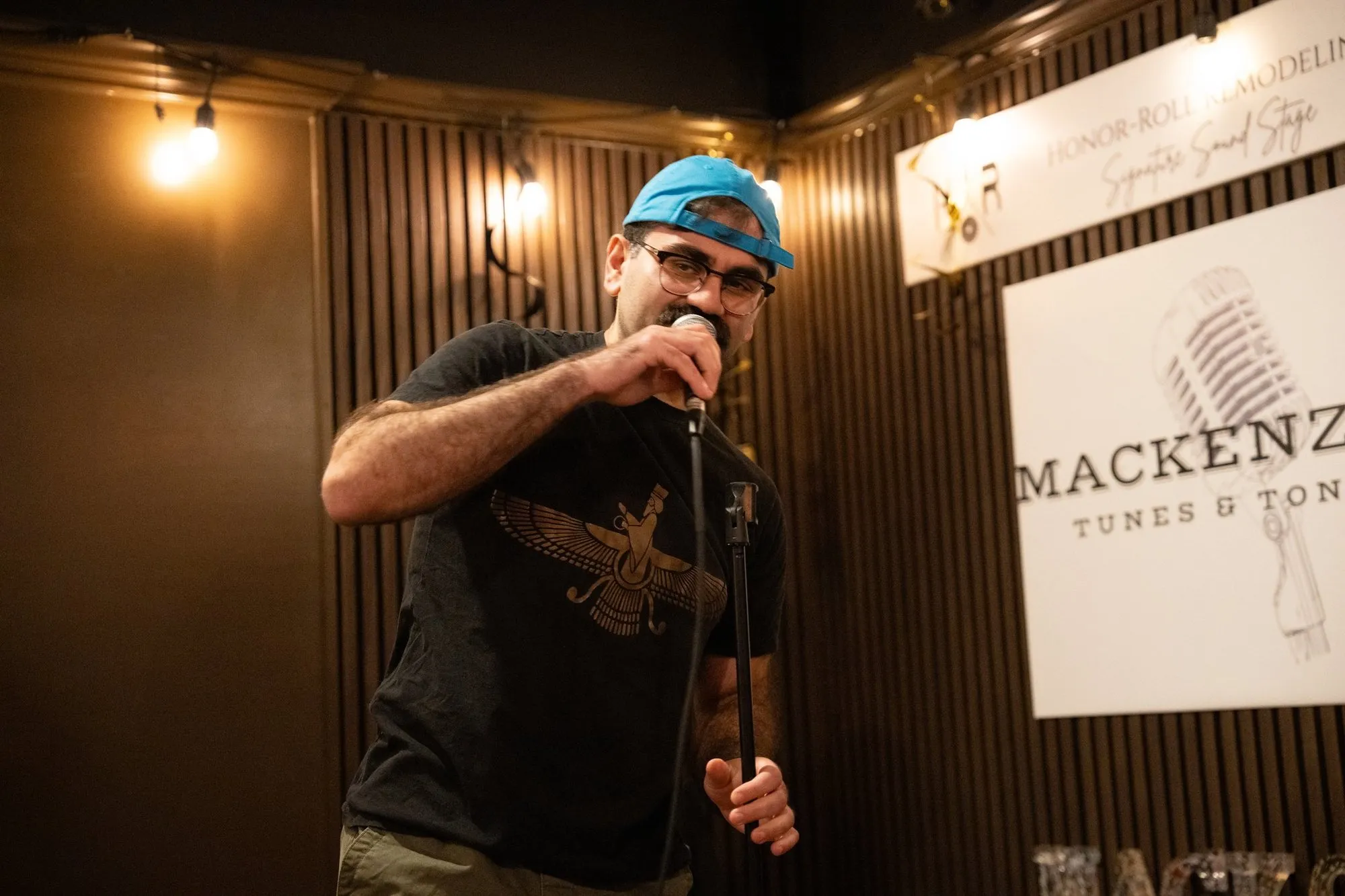 A comedian in a blue cap mid-joke