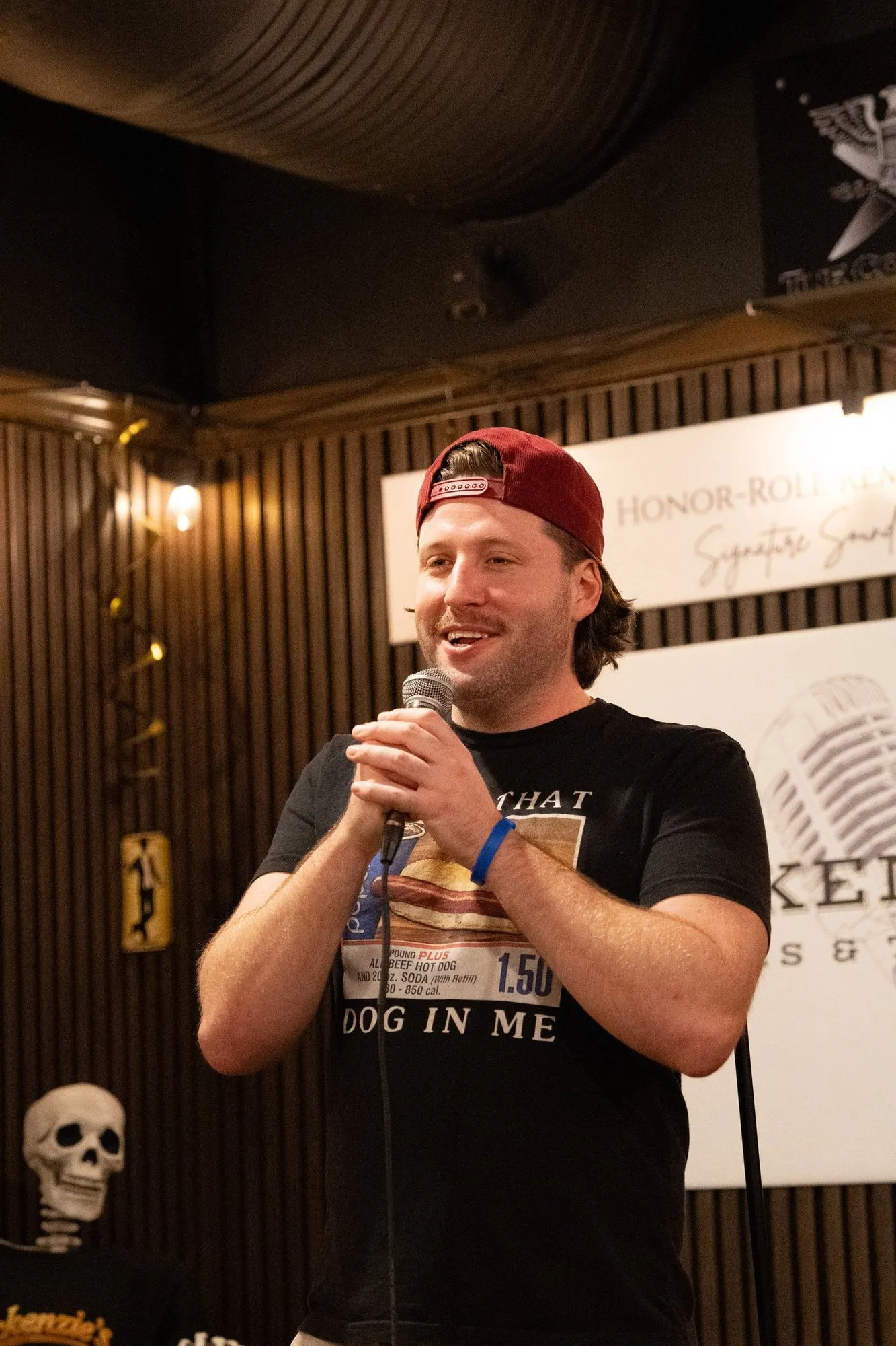 A comedian in a red cap grinning at the mic