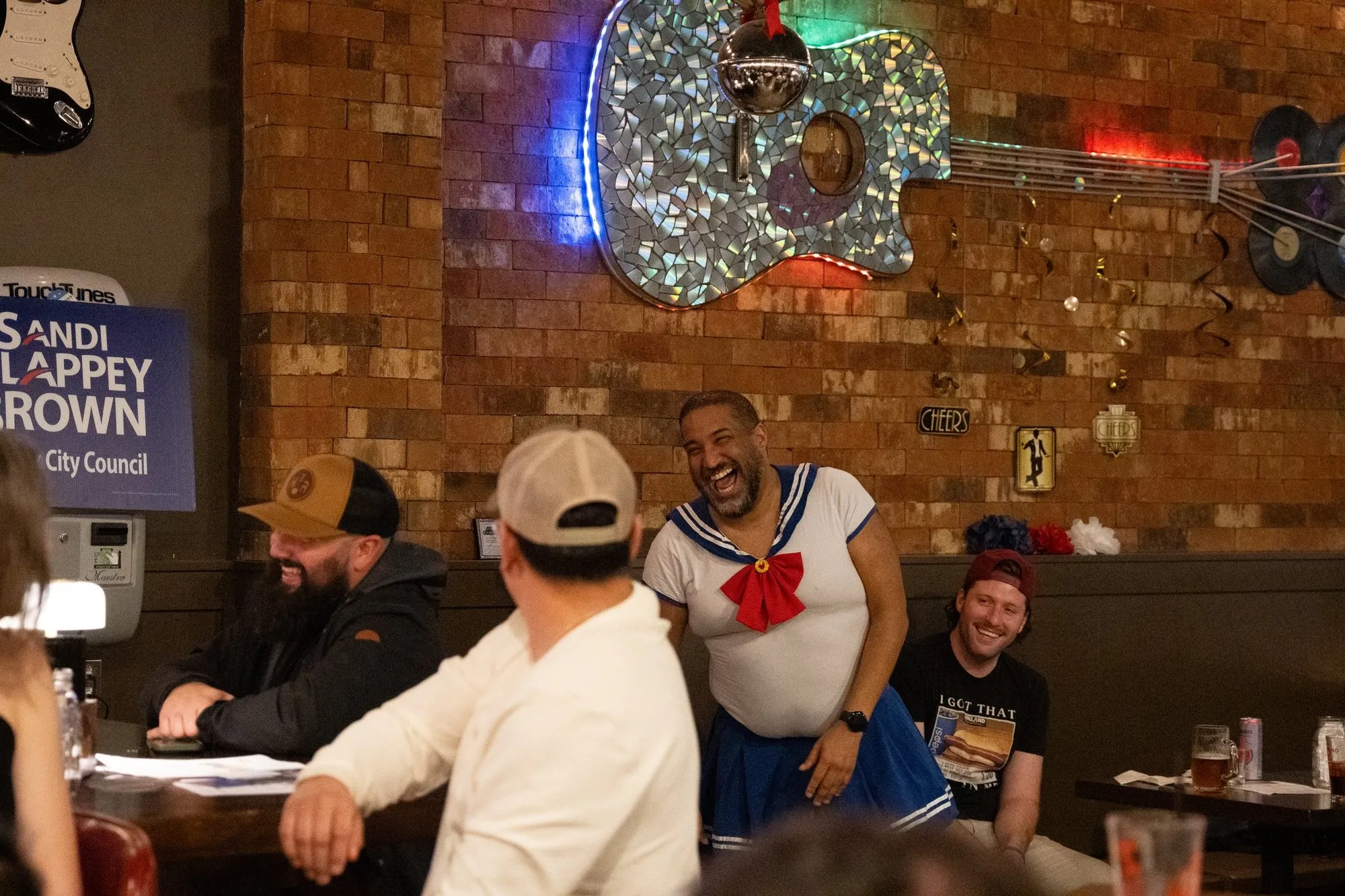 A performer in a sailor costume laughing with guests at the bar